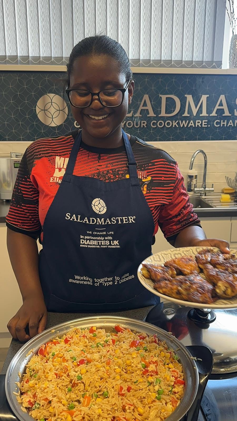 Team member in the Saladmaster Diabetes UK apron presenting jollof rice and BBQ chicken