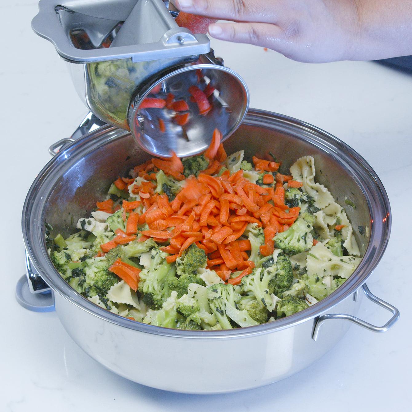 Saladmaster food processor adding fresh shredded carrots to pasta and broccoli
