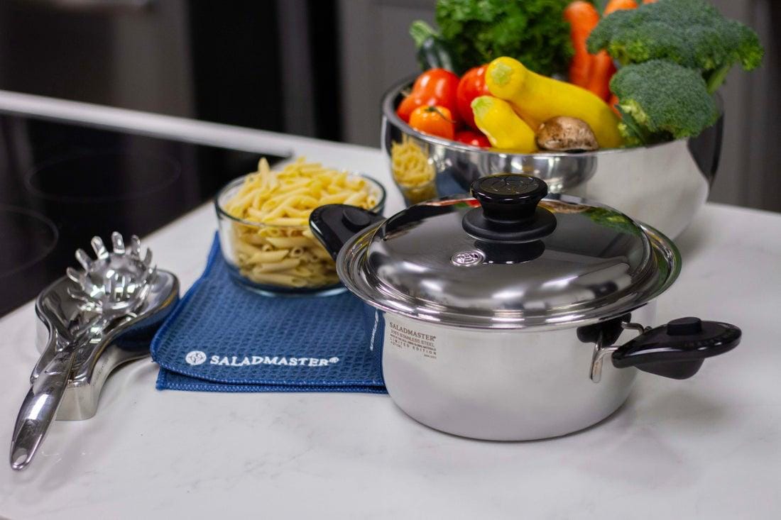 Saladmaster stainless steel cookware with fresh vegetables and pasta on a kitchen counter
