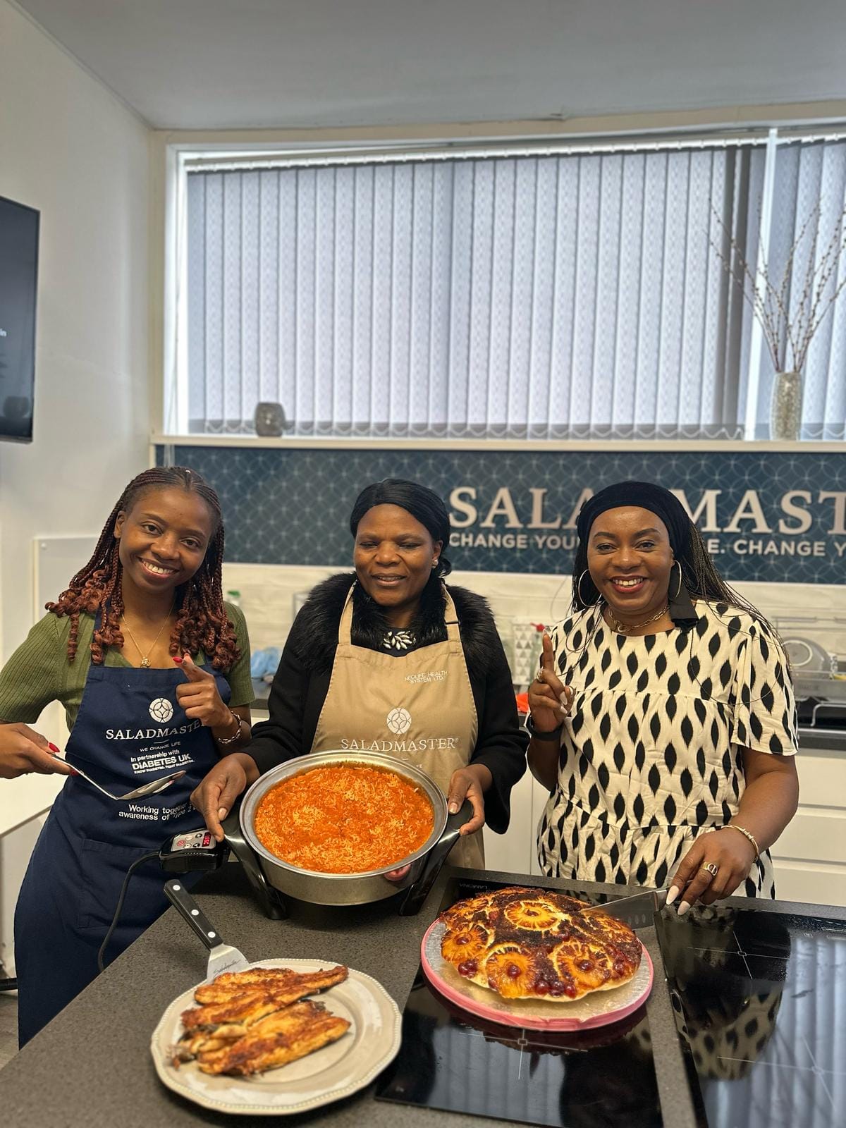 Team of three at the Strength 2 Strength Saladmaster studio holding freshly cooked jollof rice, fish and pineapple upside-down cake