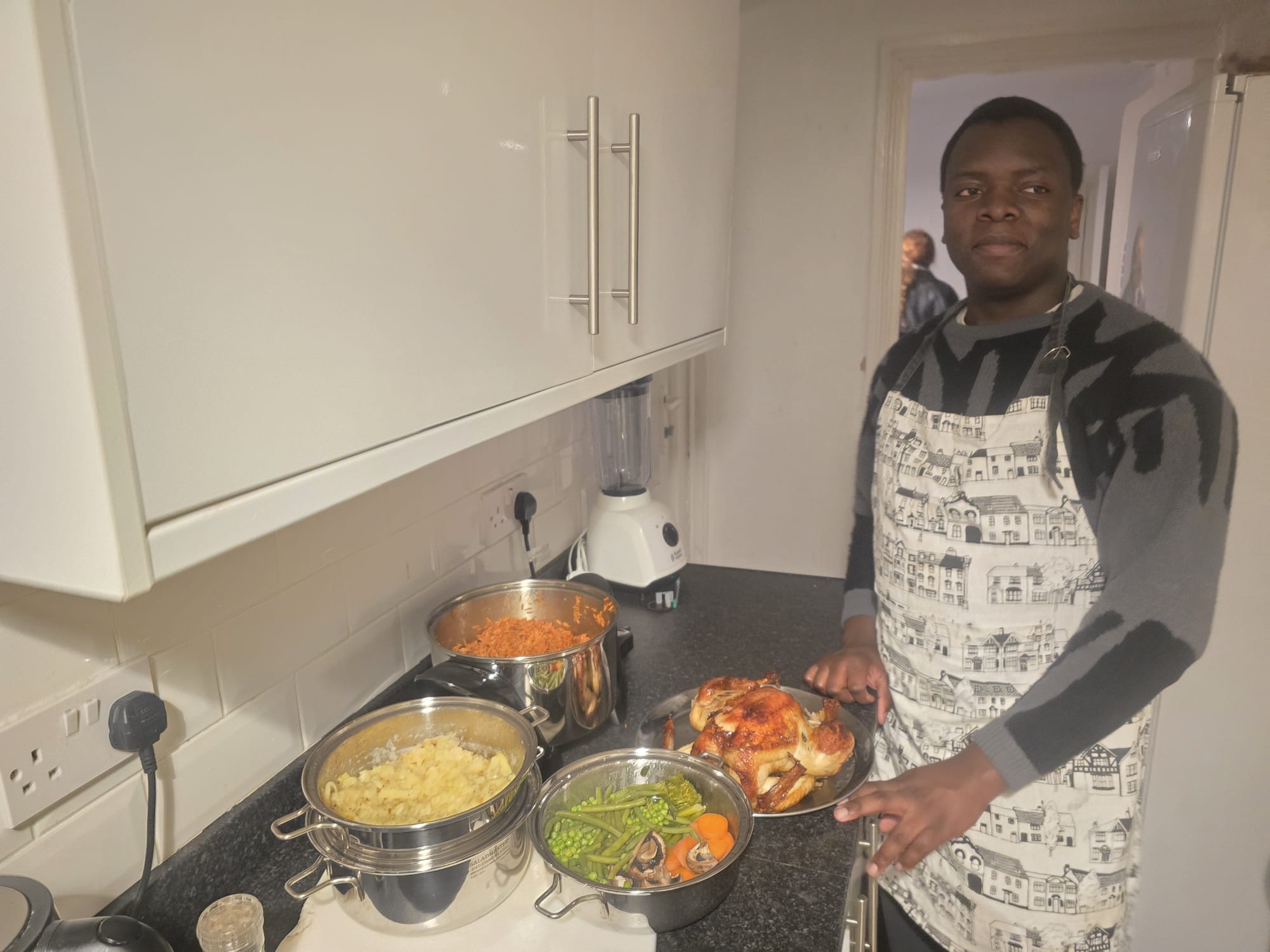 Young man in an apron presenting a roast chicken, mashed potatoes and steamed vegetables cooked in Saladmaster cookware