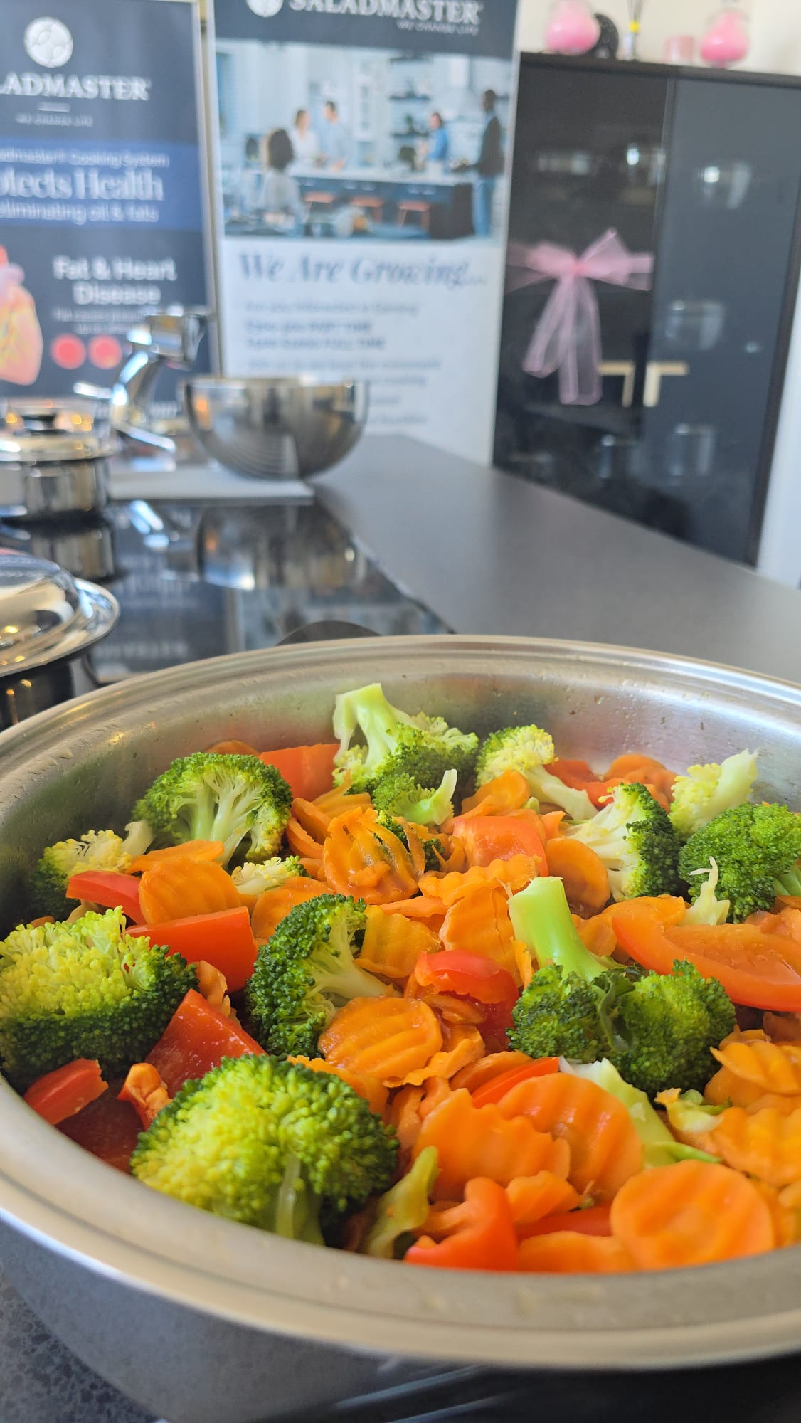 Colourful broccoli, carrots and peppers cooked without oil in a Saladmaster pan beside the Protects Health banner