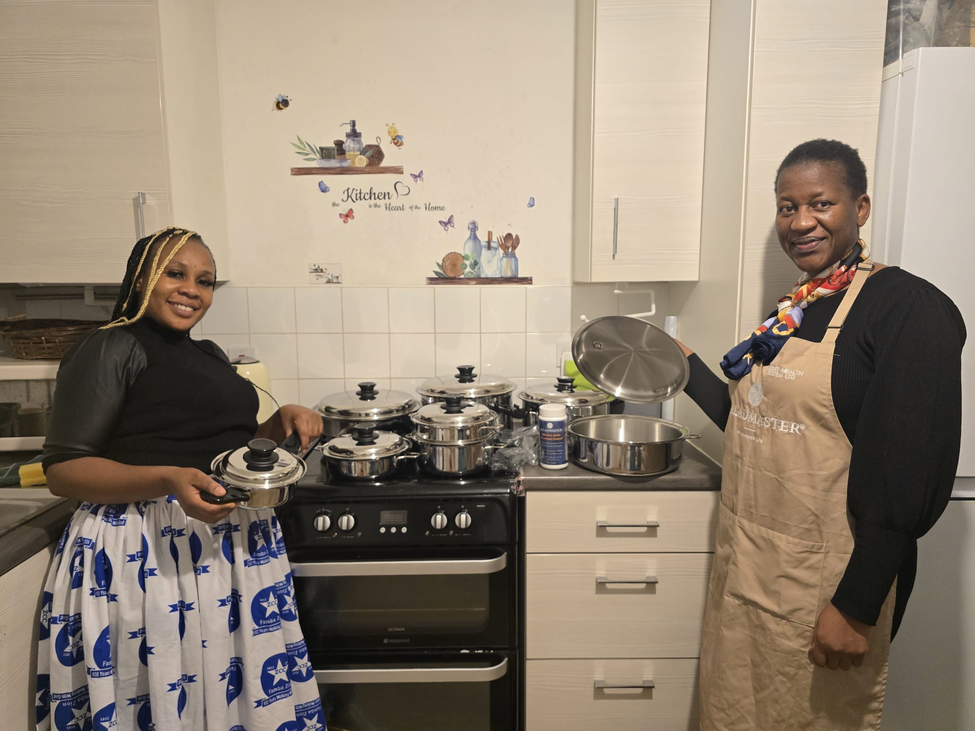 Two women in the kitchen with a full Saladmaster stainless steel cookware set on the hob