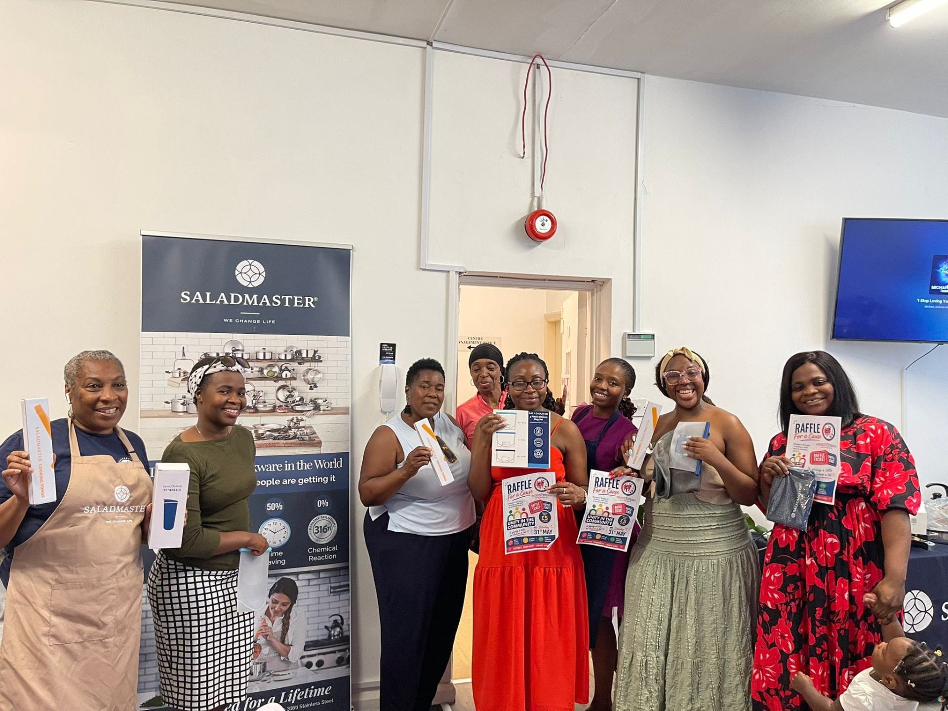 Joyful group of women holding Saladmaster gifts and Raffle for a Cause posters at a Strength 2 Strength community event